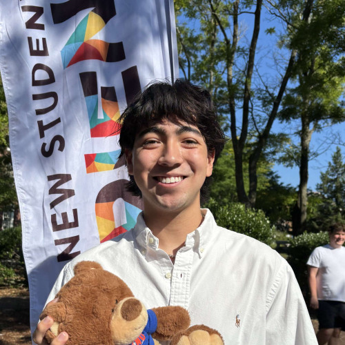 Keean smiling outside in front of a New Student Orientation flag