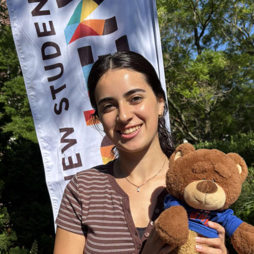 Kiana smiling outside in front of a New Student Orientation flag