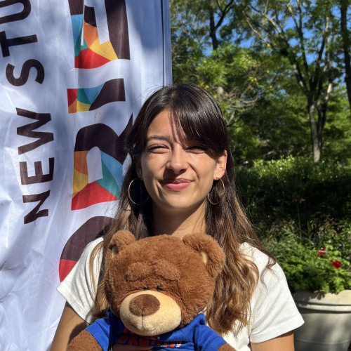 Kiera smiling outside in front of a New Student Orientation flag
