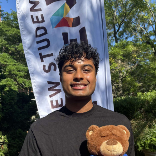 Krish smiling outside in front of a New Student Orientation flag