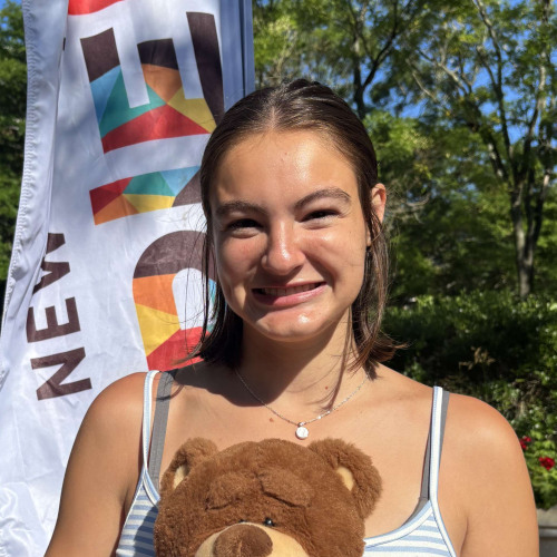 Lainey smiling outside in front of a New Student Orientation flag