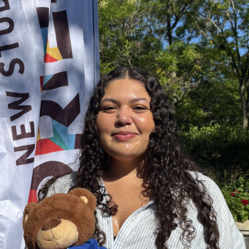 Lexie smiling outside in front of a New Student Orientation flag