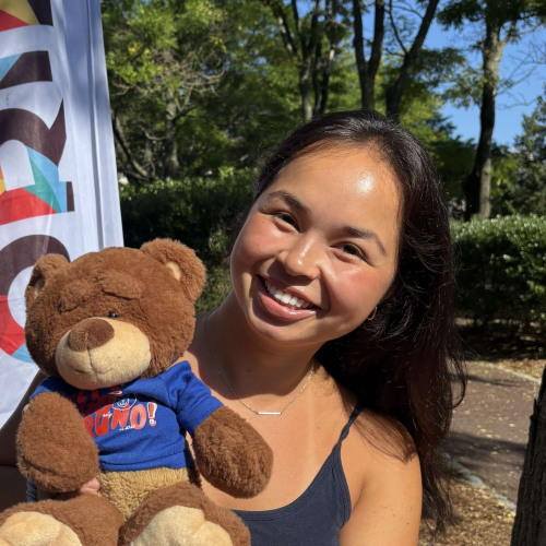 Mai smiling outside in front of a New Student Orientation flag