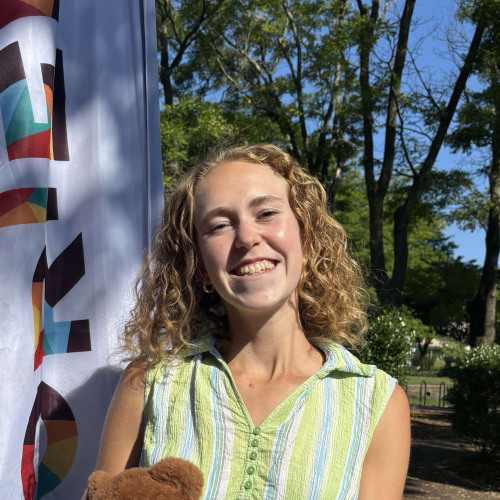 Maya smiling outside in front of a New Student Orientation flag