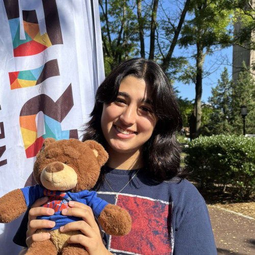 Mayan smiling outside in front of a New Student Orientation flag