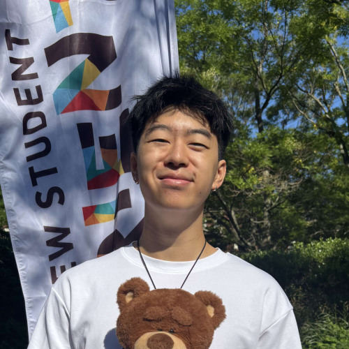 Micah smiling outside in front of a New Student Orientation flag
