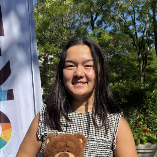 Monica smiling outside in front of a New Student Orientation flag