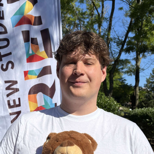 Nolan smiling outside in front of a New Student Orientation flag