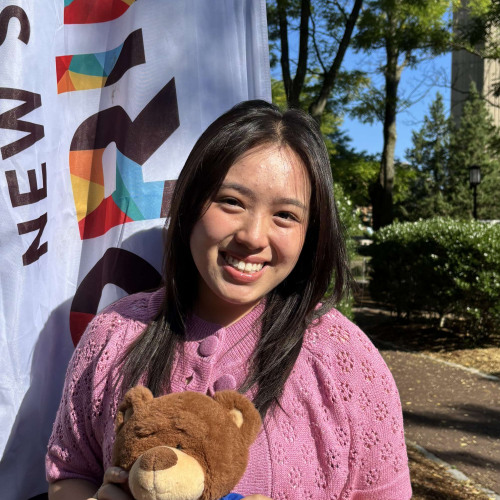 Pearl smiling outside in front of a New Student Orientation flag