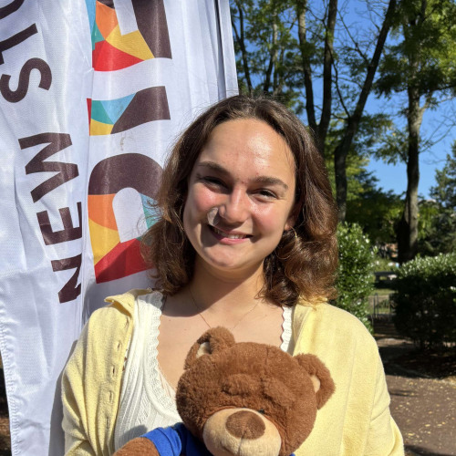 Reese smiling outside in front of a New Student Orientation flag