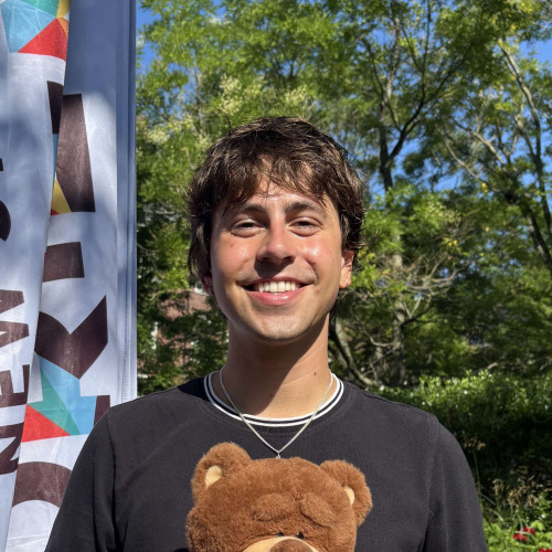 Remy smiling outside in front of a New Student Orientation flag