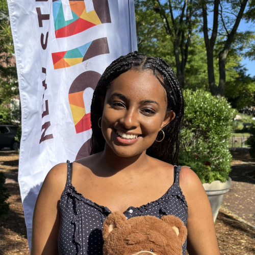 Soliyana smiling outside in front of a New Student Orientation flag