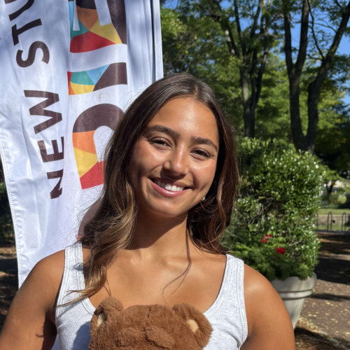 Sophie smiling outside in front of a New Student Orientation flag