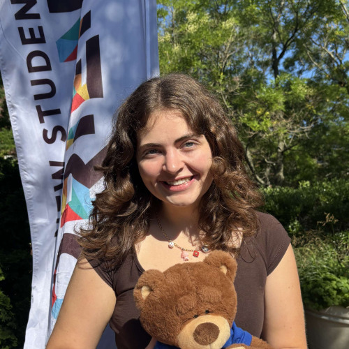 Summer smiling outside in front of a New Student Orientation flag