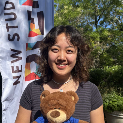 Vanessa smiling outside in front of a New Student Orientation flag