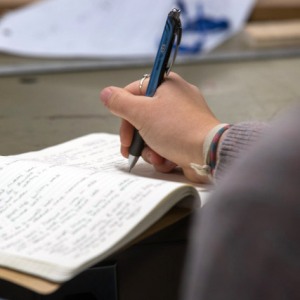 Closeup of a person writing in a lined notebook with a blue pen